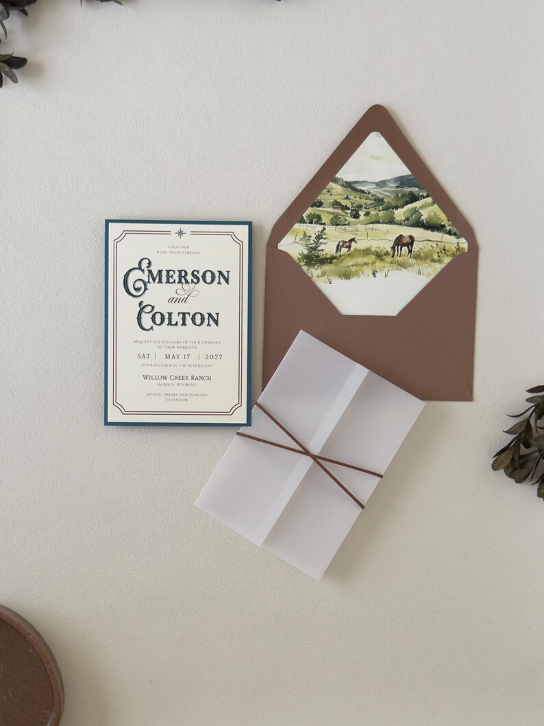 Rustic western wedding stationery featuring an ivory invitation, dusty blue details card, warm brown accents, square RSVP card and coordinating ranch landscape envelope liner.