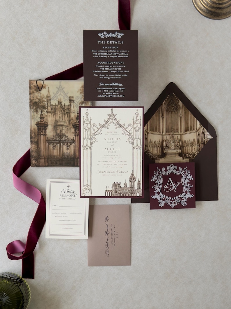 Aurelia Gothic wedding stationery featuring a cream invitation with intricate architectural artwork, Bitter Chocolate backing mat and envelope, antique-inspired Gothic interior liner, Claret decorative crest tag, and traditional RSVP stationery.