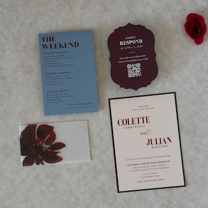 Elegant floral wedding stationery in burgundy, dusty blue and ivory, featuring an ivory invitation with deep burgundy floral artwork, blue details card, scalloped burgundy RSVP and floral envelope liner.