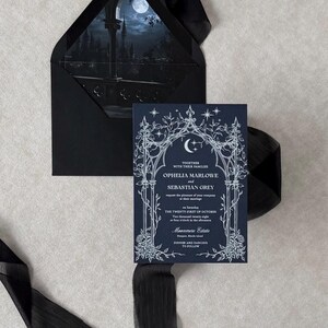 Imperial Navy wedding invitation featuring intricate white ink Gothic botanical artwork, displayed in front of an Ebony envelope with a dark blue moonlit castle liner and coordinating black ribbon.