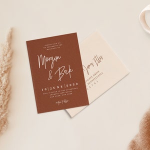 Puede incluir: Una tarjeta de invitaci&oacute;n marr&oacute;n con texto blanco anunciando el matrimonio de Morgan y Beck el 10 de junio de 2022 a las cinco de la tarde en el Gramercy Park Hotel de Nueva York. La tarjeta est&aacute; sobre una superficie blanca con un sobre beige y una tela marr&oacute;n.
