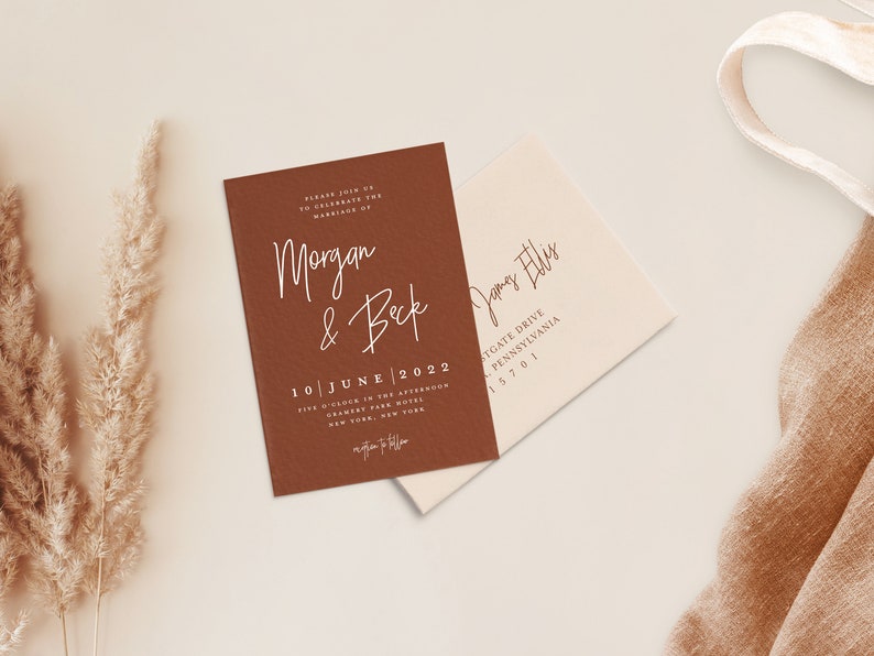 Puede incluir: Una tarjeta de invitaci&oacute;n marr&oacute;n con texto blanco anunciando el matrimonio de Morgan y Beck el 10 de junio de 2022 a las cinco de la tarde en el Gramercy Park Hotel de Nueva York. La tarjeta est&aacute; sobre una superficie blanca con un sobre beige y una tela marr&oacute;n.
