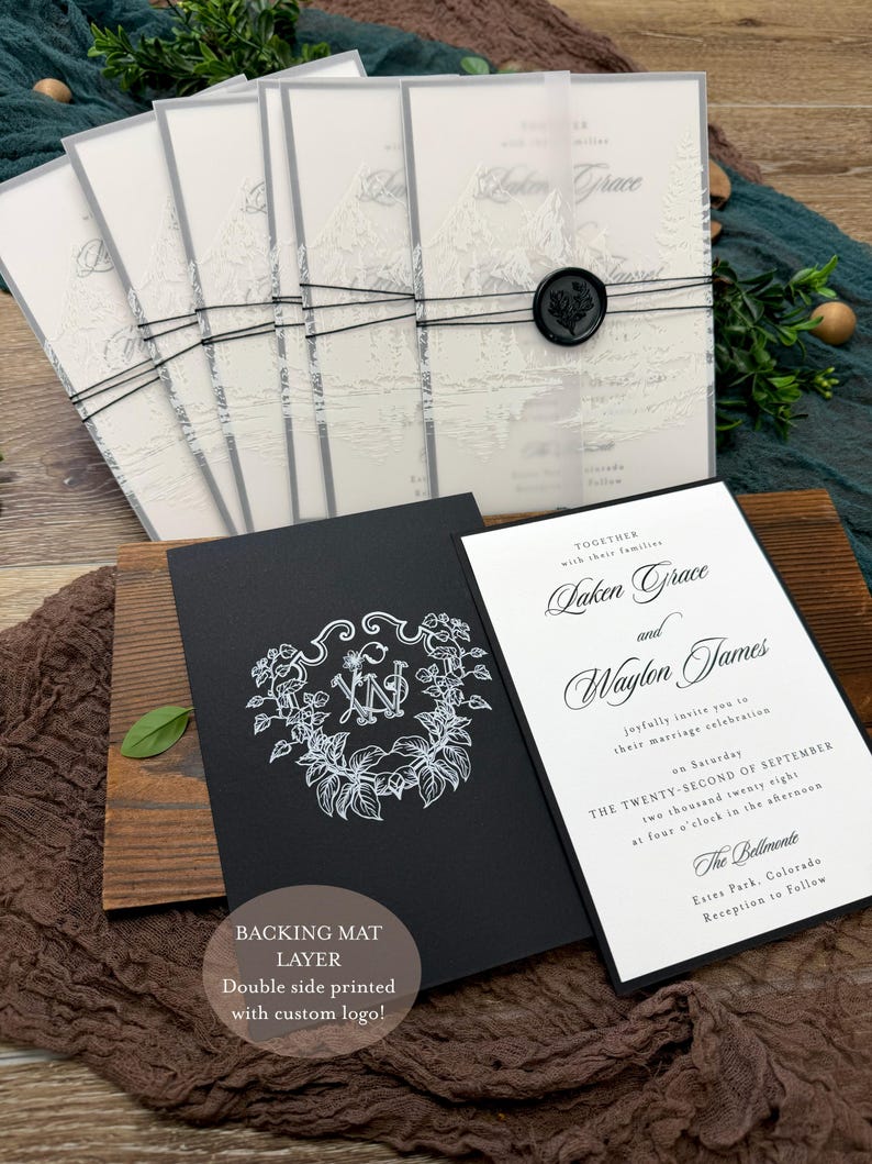 May include: Wedding invitation suite featuring a black and white design. The suite includes invitations with a mountain landscape, a black card with a floral monogram, and a white invitation with elegant script. The text reads "Laken Grace and Waylon James".