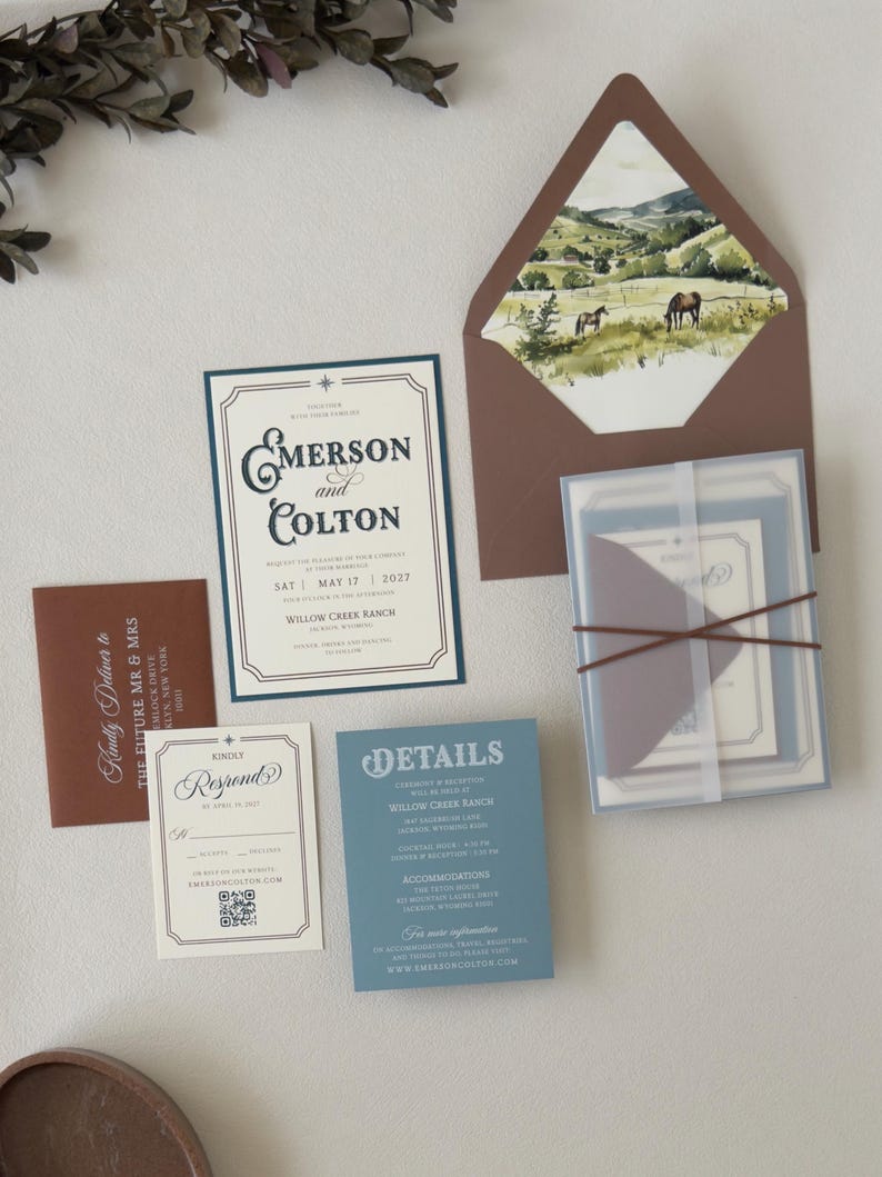 Dusty blue and brown western wedding invitation suite featuring an ivory bordered invitation, blue details card, square RSVP card and brown envelope with scenic landscape liner.