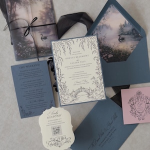 Odette wedding invitation accessories featuring a Marina blue details card, ivory botanical wedding invitation, scalloped RSVP website card, and Dusk pink decorative tag arranged with sheer black ribbon on a textured background.