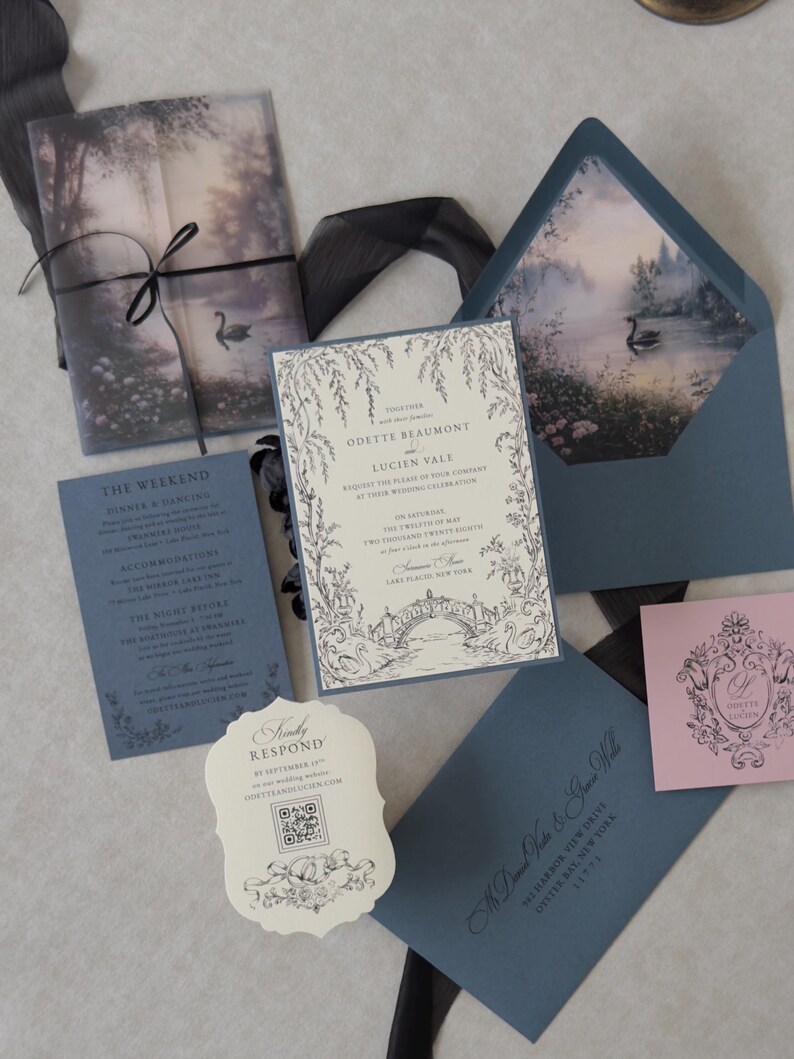 Odette wedding invitation accessories featuring a Marina blue details card, ivory botanical wedding invitation, scalloped RSVP website card, and Dusk pink decorative tag arranged with sheer black ribbon on a textured background.