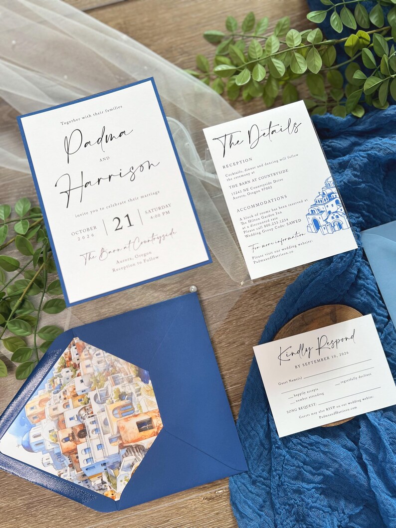 May include: Wedding invitation suite with a blue and white color scheme. The invitation features a white card with black calligraphy text that reads "Padma and Harrison" and "October 21, 2026, Saturday 4:00 PM, The Barn at Countryside, Aurora, Oregon". The details card features a blue and white illustration of a cityscape. The RSVP card features the text "Kindly Respond by September 10, 2026".