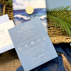 May include: Wedding invitation suite featuring a blue and white watercolor design with ocean waves and a full moon. The invitation includes details about the venue, schedule of events, and accommodations. A gold wax seal adds an elegant touch.