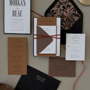 Complete modern Whitmore wedding stationery suite featuring bold black typography, layered invitation, rust brown details cards, black envelope and thin ribbon accents.