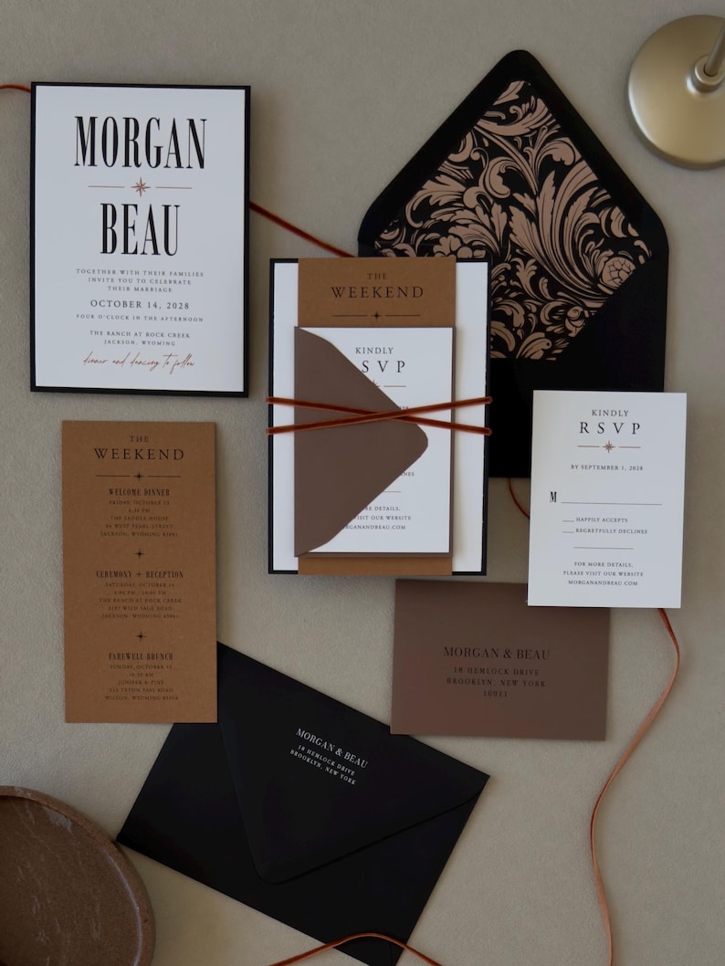Complete modern Whitmore wedding stationery suite featuring bold black typography, layered invitation, rust brown details cards, black envelope and thin ribbon accents.