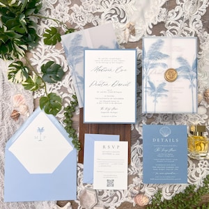 May include: A collection of light blue and white wedding stationery, including invitations, RSVP cards, and details cards. The invitations feature palm tree illustrations and elegant script. A gold wax seal and seashells add decorative touches.
