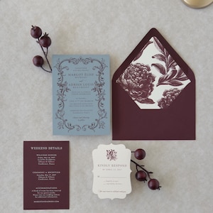 Close-up of premium wedding stationery in dusty blue, burgundy and ivory with scalloped and botanical design details