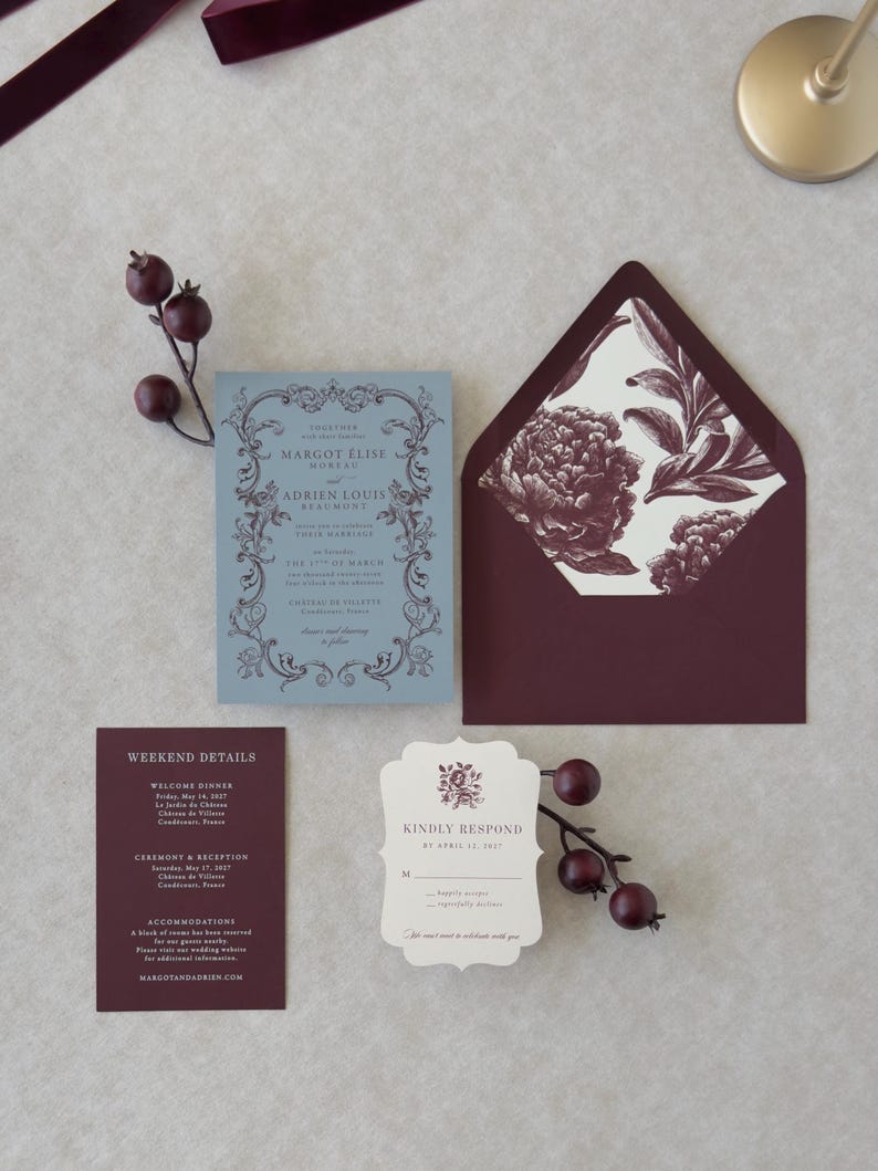 Close-up of premium wedding stationery in dusty blue, burgundy and ivory with scalloped and botanical design details