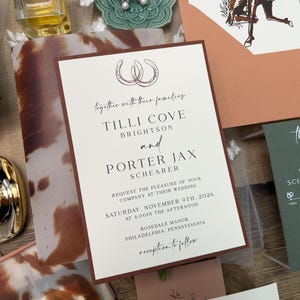 May include: Wedding invitation suite with a rustic theme. The invitation features a brown border and text that reads "Tilli Cove Brightson and Porter Jax Schearer". Other elements include a perfume bottle, a green ceramic dish with earrings, and a cowhide pattern.