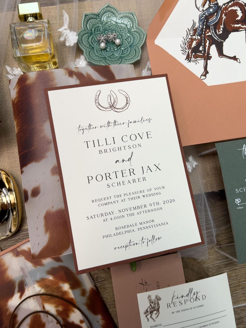 May include: Wedding invitation suite with a rustic theme. The invitation features a brown border and text that reads "Tilli Cove Brightson and Porter Jax Schearer". Other elements include a perfume bottle, a green ceramic dish with earrings, and a cowhide pattern.
