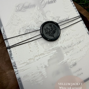 May include: A vellum jacket with white ink printing, featuring a mountain and forest design. The invitation is secured with black twine and a black wax seal with a botanical design. Text on the image reads "Vellum jacket, White ink printed, Included with all suites!"