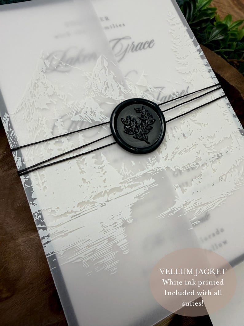 May include: A vellum jacket with white ink printing, featuring a mountain and forest design. The invitation is secured with black twine and a black wax seal with a botanical design. Text on the image reads "Vellum jacket, White ink printed, Included with all suites!"