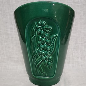 May include: A green ceramic planter with a raised design of a lily of the valley flower.