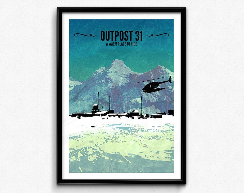 May include: Framed art print depicting a mountain scene with a helicopter and silhouetted structures. The text "OUTPOST 31" and "A warm place to hide" are at the top. The print uses a colour palette of blues, greens, and white, evoking a cold environment.