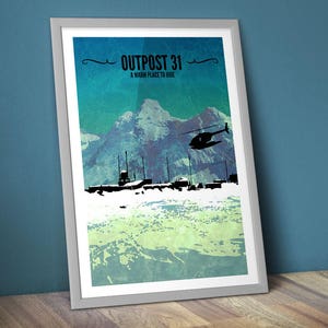 May include: Framed art print depicting a mountain scene with a helicopter and buildings in silhouette. The text "OUTPOST 31" and "A warm place to hide" are at the top. The artwork uses a blue, green, and white colour scheme.