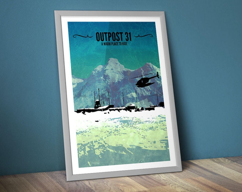 May include: Framed art print depicting a mountain scene with a helicopter and buildings in silhouette. The text "OUTPOST 31" and "A warm place to hide" are at the top. The artwork uses a blue, green, and white colour scheme.