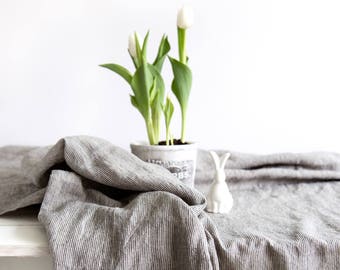 Op de afbeelding: Een grijs-wit gestreept linnen tafelkleed met een wit keramiek konijn en een potplant met witte tulpen.