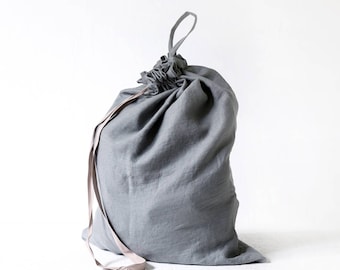 May include: A large grey drawstring bag made of soft fabric. The bag has a gathered top with a loop handle and a light-coloured drawstring. The bag is designed to hold items and is suitable for storage or travel.