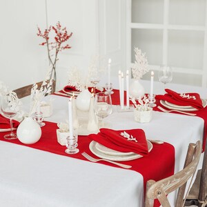 May include: A white tablecloth with red placemats and white napkins. There are white vases with white flowers and candles on the table. The table is set for a formal dinner.
