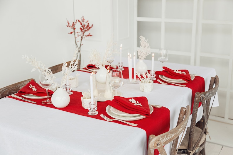 May include: A white tablecloth with red placemats and white napkins. There are white vases with white flowers and candles on the table. The table is set for a formal dinner.