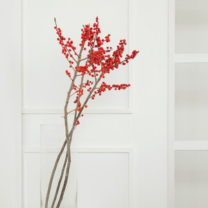 May include: A clear glass vase with red berries and thin branches on a white pedestal.