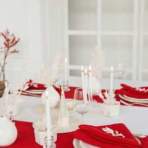 May include: A white table setting with red napkins, white plates, and white candles. The table is decorated with white flowers and greenery.