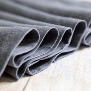May include: Close-up of a folded gray fabric with a smooth texture. The fabric is folded in a way that creates a series of curves and lines.