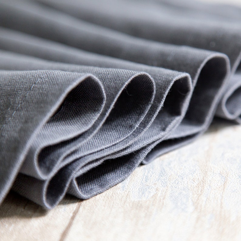 May include: Close-up of a folded gray fabric with a smooth texture. The fabric is folded in a way that creates a series of curves and lines.