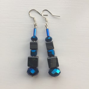 May include: A pair of dangle earrings with black and blue iridescent glass beads. The earrings have silver hooks.