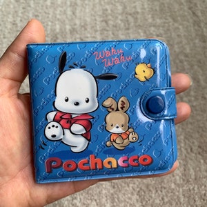 May include: A blue wallet with a cartoon character of Pochacco, a white dog with a red shirt, and a rabbit with an orange shirt. The wallet has a blue button closure and the text "Waku Waku" and "Pochacco" printed on it.