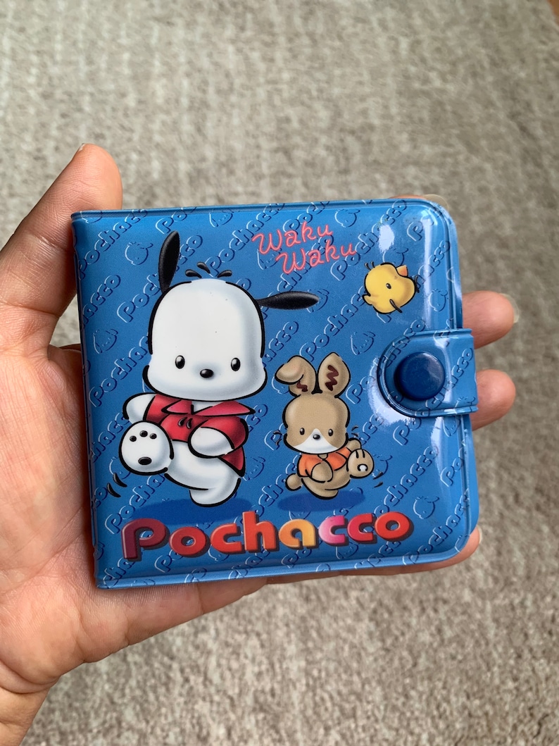 May include: A blue wallet with a cartoon character of Pochacco, a white dog with a red shirt, and a rabbit with an orange shirt. The wallet has a blue button closure and the text "Waku Waku" and "Pochacco" printed on it.