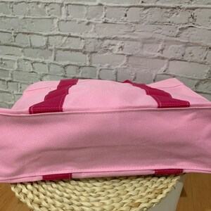 K&ouml;nnte beinhalten: Eine rosa Canvas-Tragetasche mit roten Streifen. Die Tasche ist aus einem weichen, strapazierf&auml;higen Material gefertigt und hat ein ger&auml;umiges Innenleben.