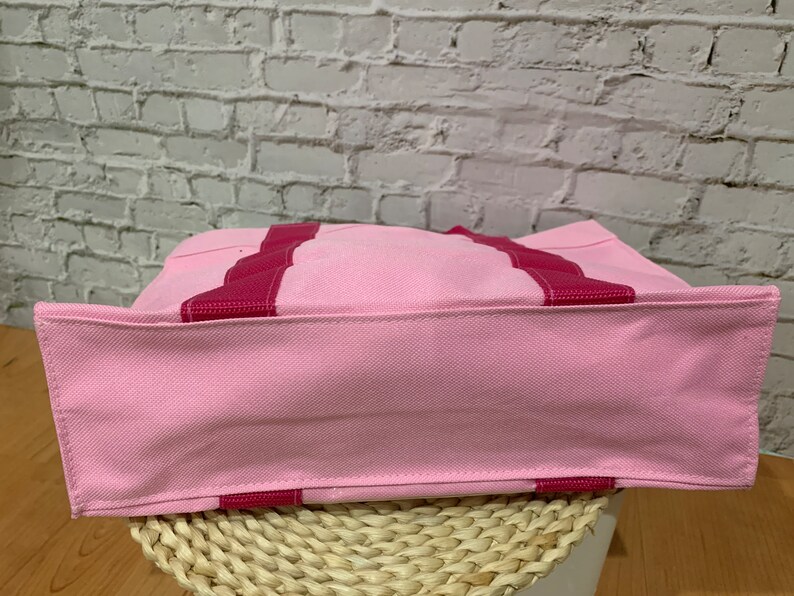 K&ouml;nnte beinhalten: Eine rosa Canvas-Tragetasche mit roten Streifen. Die Tasche ist aus einem weichen, strapazierf&auml;higen Material gefertigt und hat ein ger&auml;umiges Innenleben.