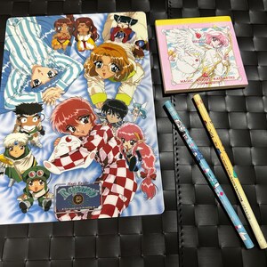 May include: A colourful illustration of a group of anime characters, including a red-haired girl wearing a chequered kimono, a blue-haired boy in pyjamas, and a pink-haired girl with wings. The illustration is on a blue background with white clouds. The text "Magic Knight Rayearth" is visible in the bottom right corner.