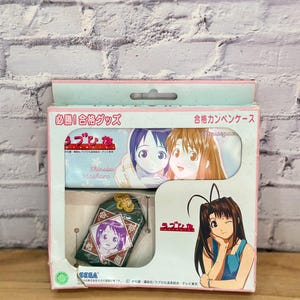 以下が含まれることがあります： アニメのキャラクターと日本語のテキストが特徴の箱入りセット。箱にはペンケースと小さな緑色の装飾品が入っています。箱はピンクと白の配色で、白いレンガの壁を背景にしています。