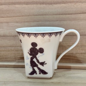 May include: White ceramic mug featuring a black silhouette of Minnie Mouse in a vintage-inspired design. The mug has a square base and a handle.