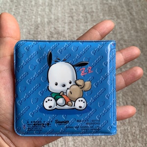 May include: A blue plastic coin purse with a white cartoon dog and a brown bunny. The purse has a repeating pattern of the dog's name "Pochacco" on the front and back. The purse has the text "Sanrio Smiles" and "450JXTOYO" on the bottom.