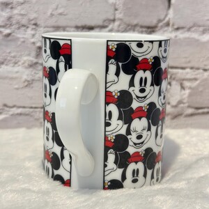 Puede incluir: Taza de cer&aacute;mica blanca con un patr&oacute;n repetido de caras de Mickey y Minnie Mouse. Los personajes son en blanco, negro y rojo, con Minnie usando un sombrero rojo. La taza tiene un asa blanca y un acabado brillante.