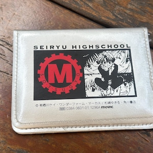 以下が含まれることがあります： 「SEIRYU HIGHSCHOOL」の文字と赤と黒のグラフィックが入ったシルバーカラーのカードケース。グラフィックには「M」の文字と、アニメスタイルのキャラクターのイラストが含まれています。追加の日本語テキストも表示されています。