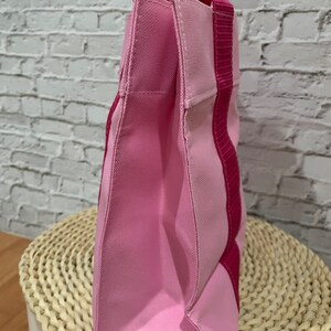K&ouml;nnte beinhalten: Eine rosa und fuchsiafarbene Tragetasche mit einem einzigen Henkel. Die Tasche ist aus Canvas gefertigt und hat ein schlichtes Design.