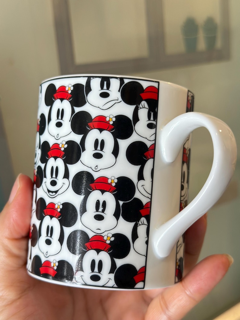 Puede incluir: Taza de cer&aacute;mica blanca con un patr&oacute;n repetido de caras de Mickey Mouse con sombreros rojos y orejas negras. La taza tiene un asa blanca y un borde negro. Un dise&ntilde;o alegre para los fan&aacute;ticos de Disney.