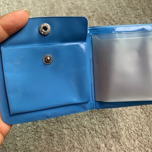 May include: A blue plastic wallet with two clear plastic pockets. The wallet has two silver metal snaps.