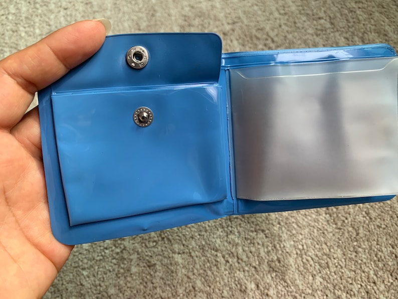May include: A blue plastic wallet with two clear plastic pockets. The wallet has two silver metal snaps.