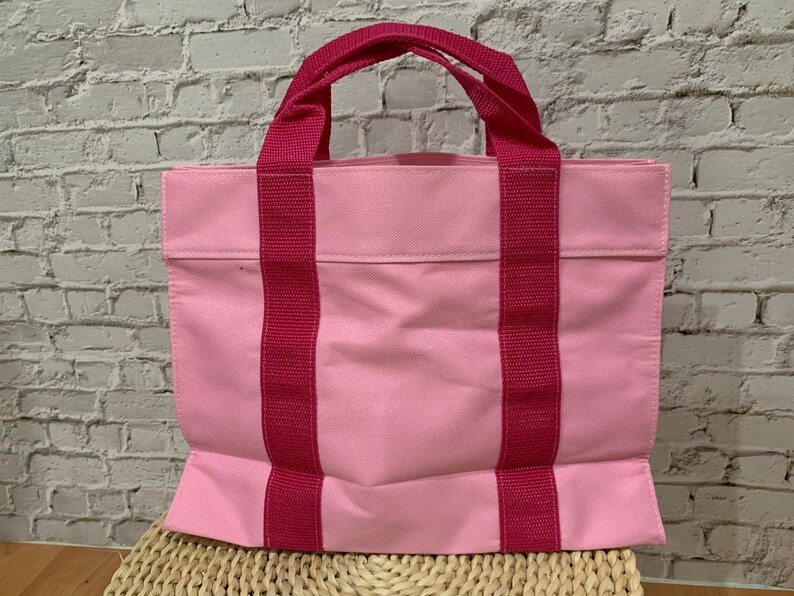 K&ouml;nnte beinhalten: Eine rosa Canvas-Tragetasche mit zwei dicken rosa Henkeln. Die Tasche hat eine einzelne Tasche auf der Vorderseite.