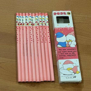 May include: A pack of 12 pink pencils with a cartoon duck design. The pencils are labeled "Patsy Duck" and "かきかた 2B". The packaging features a cartoon duck in a blue hat and a white hat.